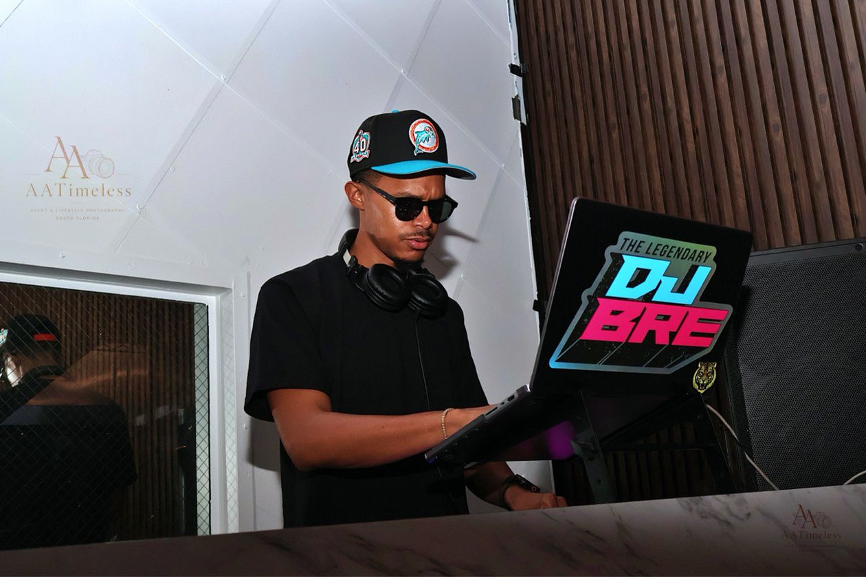 DJ BRE performing in a DJ booth with his signature laptop