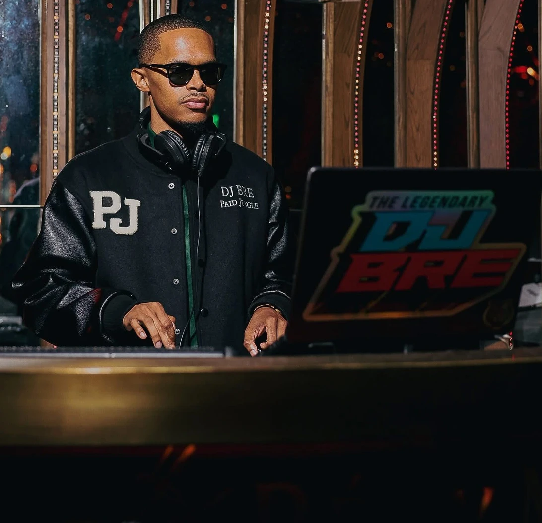DJ BRE performing behind the booth in a Paid Jungle jacket