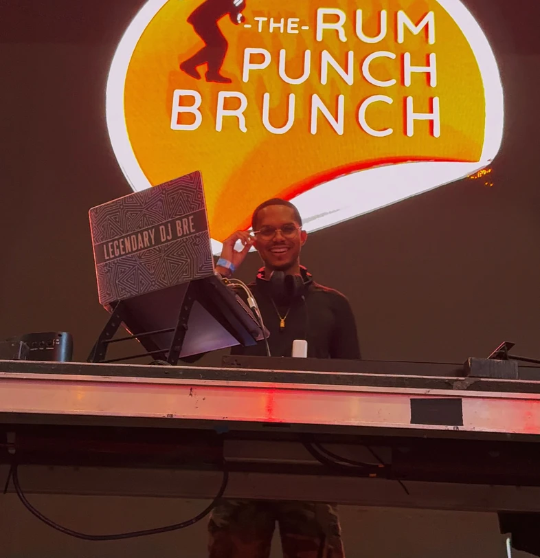 DJ BRE smiling behind the DJ booth at Rum Punch Brunch
